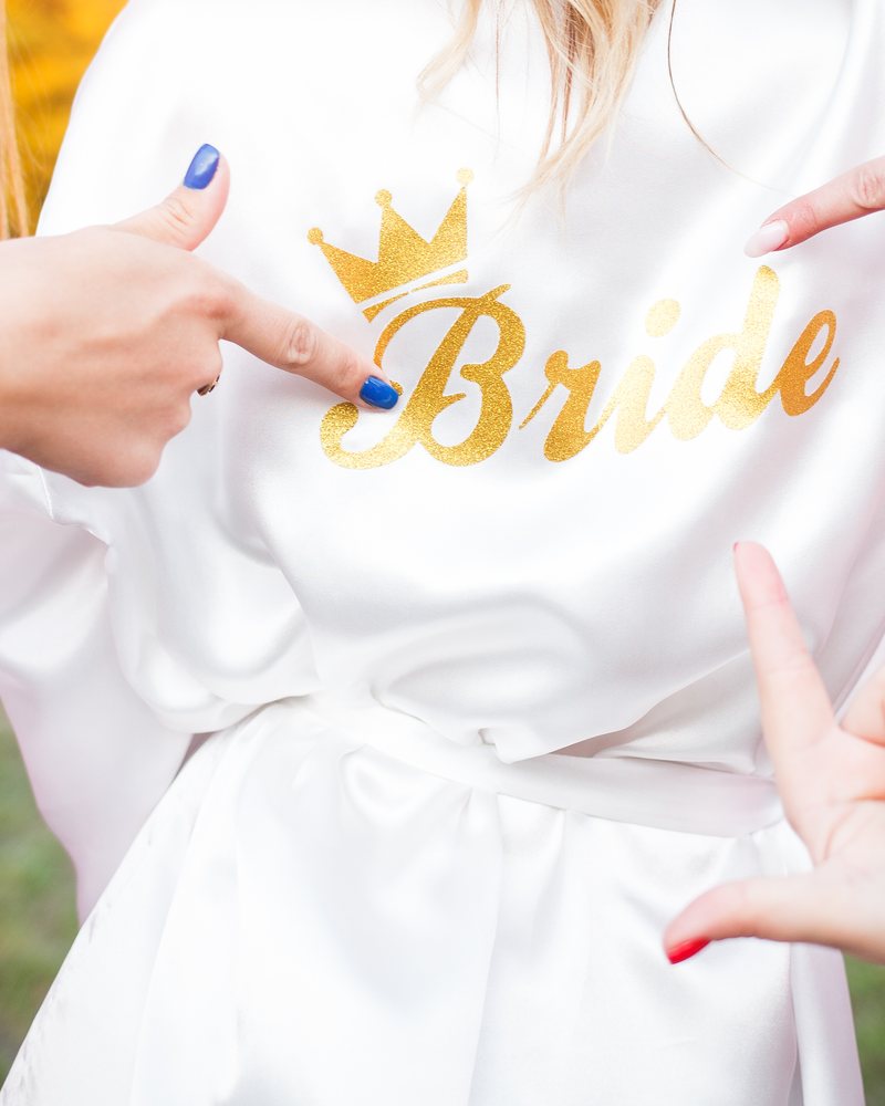 Goldener Bride-Aufdruck auf einem weißen Shirt, umgeben von zeigenden Händen
